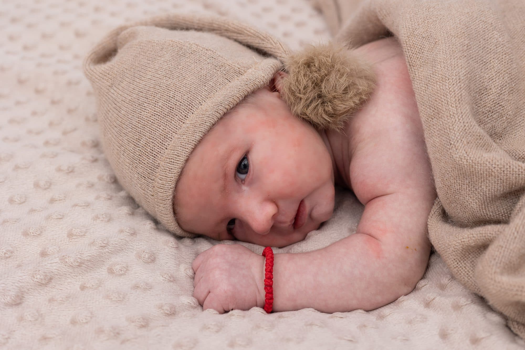 Baby mit offenen Augen und Mütze auf Decke